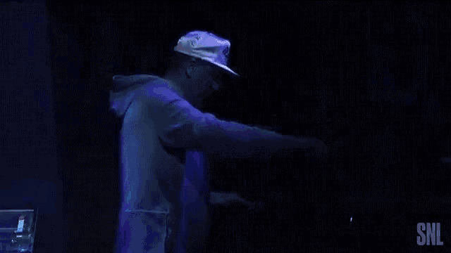 a man in a white hat is dancing in a dark room