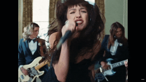 a woman in a black dress is singing into a microphone in front of a band