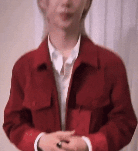 a man wearing a red jacket and a white shirt is standing in front of a white curtain .