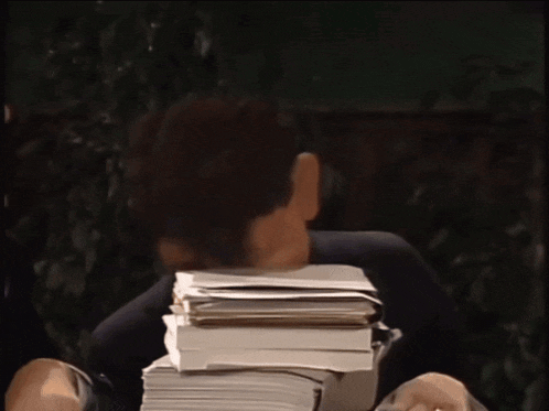a man is sitting at a desk with a stack of papers on his face