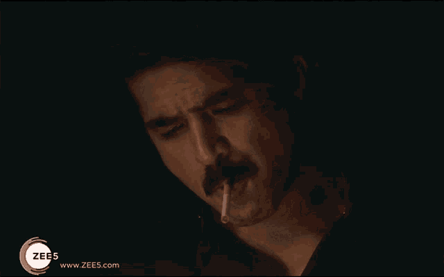 a man with a mustache is smoking a cigarette with the website www.zee5.com in the corner