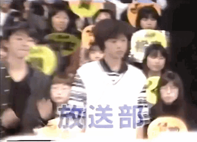 a man in a white shirt stands in front of a crowd with chinese writing on the bottom