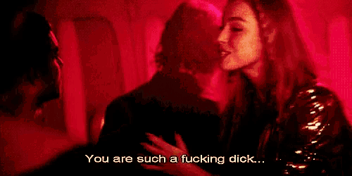 a woman is standing in a dark room with a red background and says `` you are such a fucking dick ... ''