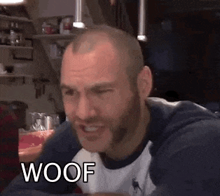 a man with a beard is making a funny face while sitting at a table with the word woof on his face .