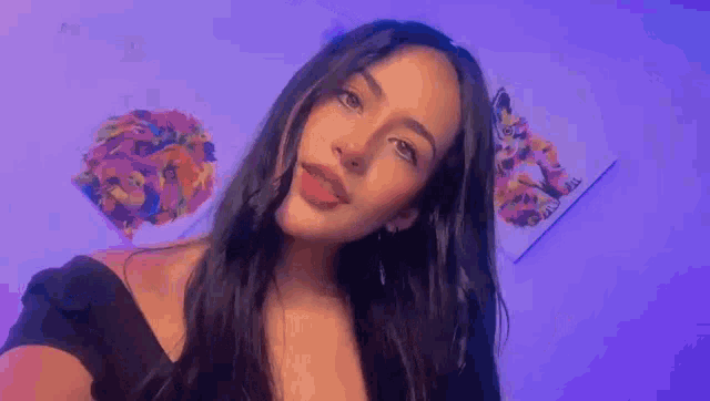 a young woman with long dark hair is taking a selfie in front of a purple wall .