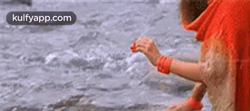 a woman in a red dress is standing in a body of water holding something in her hand .