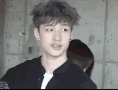 a young man with gray hair is standing in a room with a woman behind him .