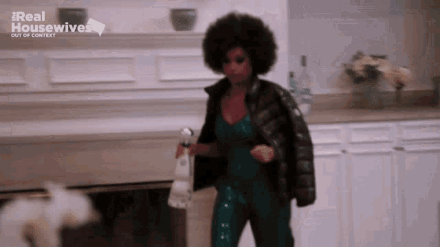 a woman in a green jumpsuit is holding a spray bottle in front of the real housewives logo