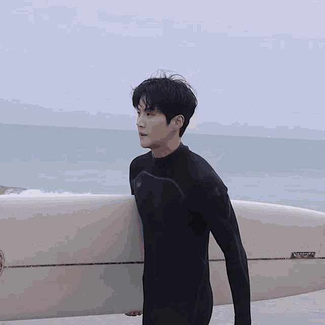 a young man in a wetsuit carrying a surfboard