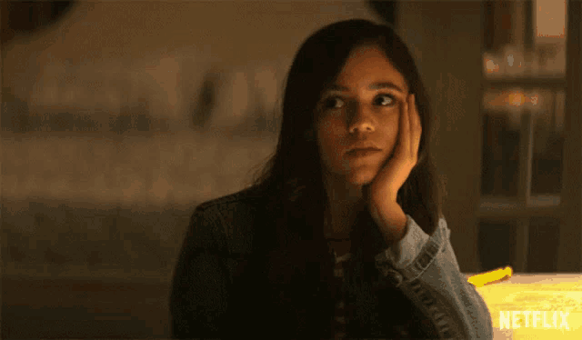 a girl is sitting at a table with her hand on her face and the word netflix is on the bottom