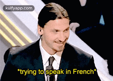 a man in a suit and tie is smiling and says " trying to speak in french "