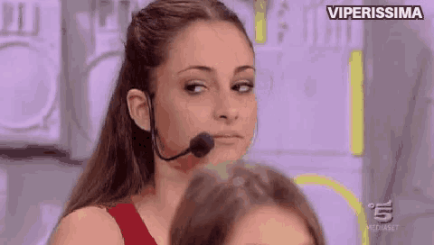 a woman with a microphone on her head is looking at the camera .