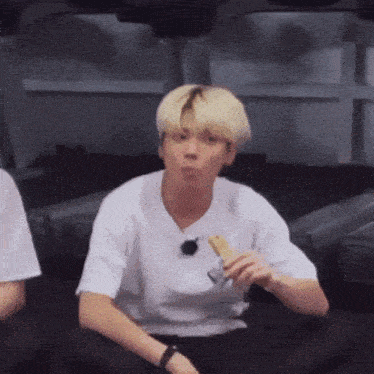 a young man in a white shirt is sitting on a couch eating a snack .