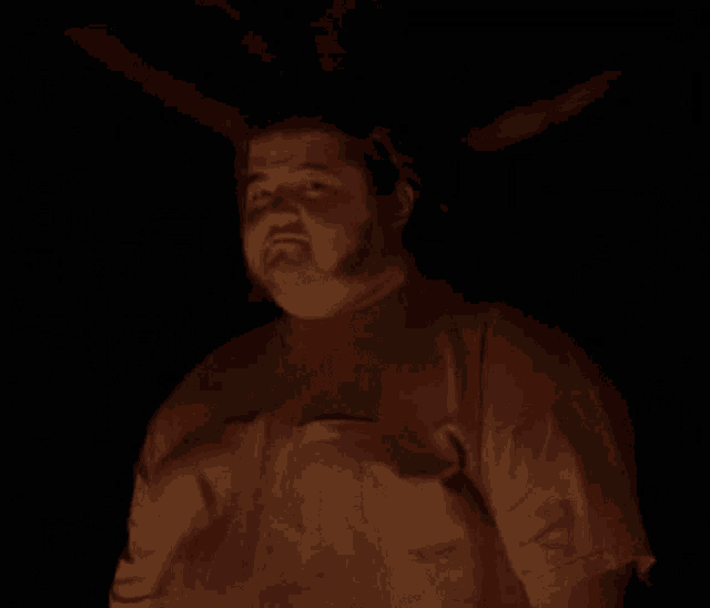 a man in a red shirt is giving a thumbs up in the dark