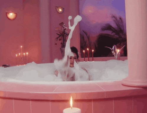 a woman is taking a bath in a tub with candles in the background