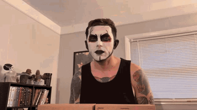 a man with white paint on his face is sitting in front of a cardboard box