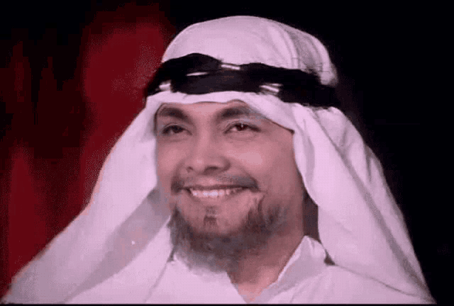 a man with a beard is wearing a white scarf and smiling .