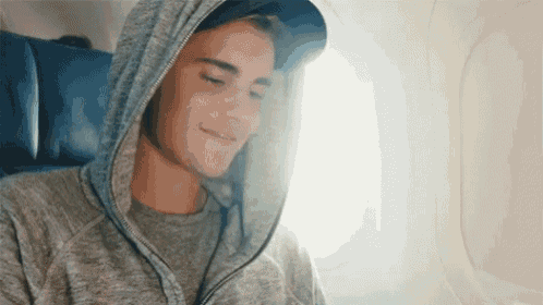 a man wearing a hooded sweatshirt is sitting on an airplane
