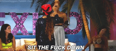 a group of women are standing in front of a sign that says " sit the fuck down " ..