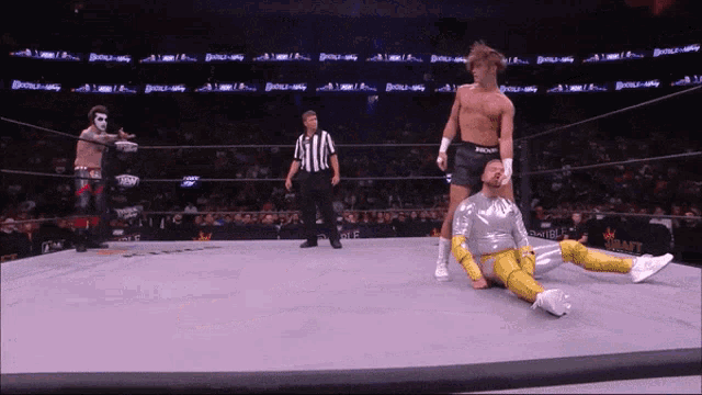 a wrestler is laying on the ground while a referee stands behind him