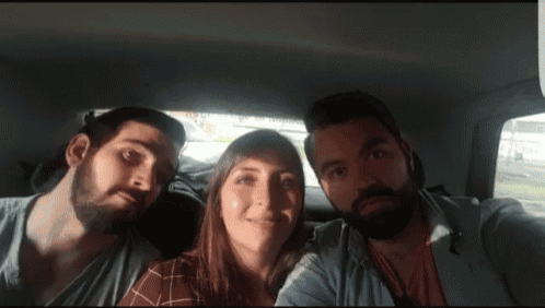 two men and a woman pose for a picture in the back seat of a car