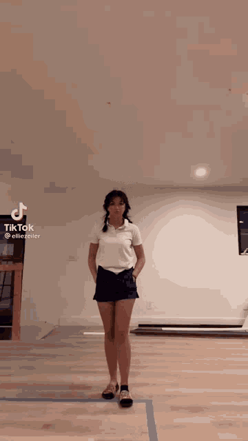 a woman in a white shirt and blue shorts is standing on a wooden floor .