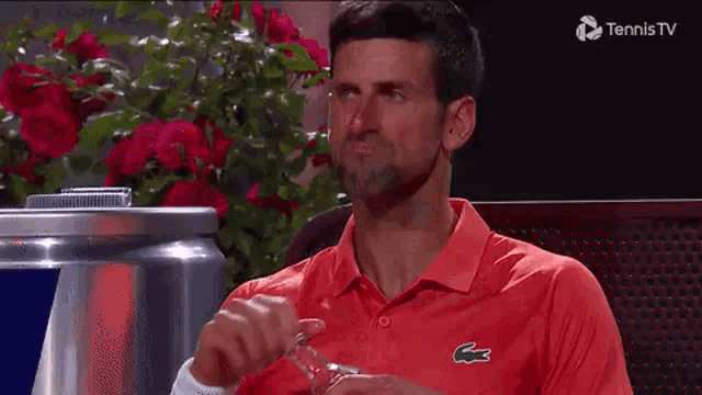 a man in a red shirt with a lacoste logo on it is drinking from a glass .