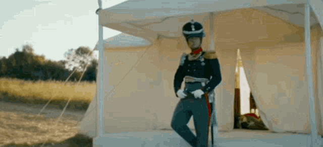a man in a military uniform is standing in front of a tent in a field .