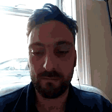 a man with a beard has his eyes closed in front of a window