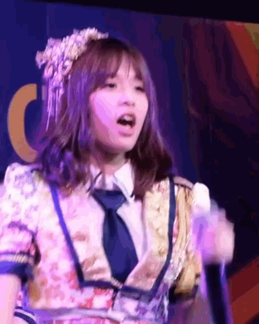 a girl in a floral dress and tie is singing into a microphone