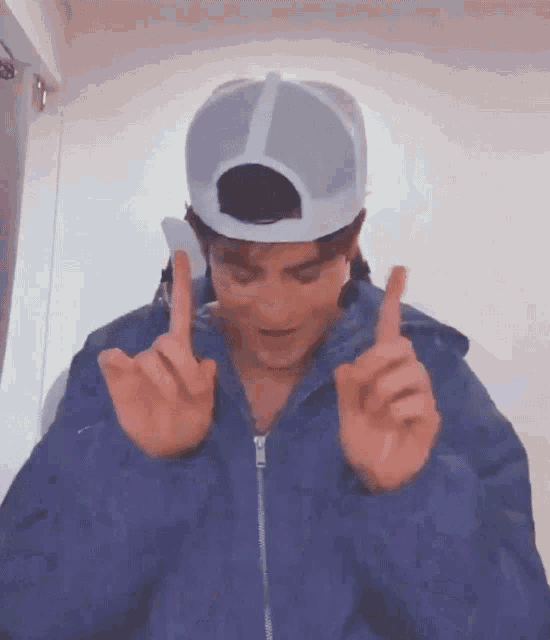 a man wearing a blue jacket and a hat is giving the middle finger .