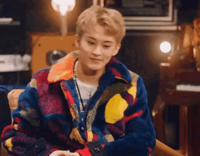 a young man wearing a colorful jacket is sitting in a chair in a room .