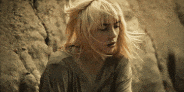 a woman with blonde hair is sitting on a rock looking down