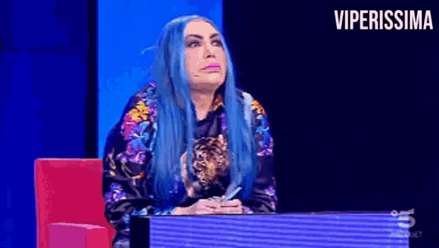 a woman with blue hair is sitting in front of a screen with the word viperissima on it
