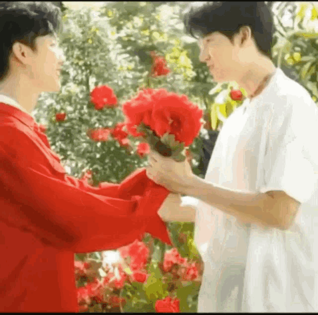 a man in a red jacket is giving a bouquet of red flowers to another man in a white shirt .