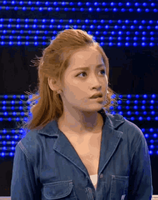 a woman in a denim jacket is looking at the camera