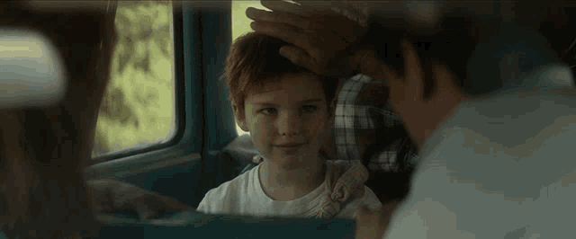 a young boy with red hair is sitting in the back seat of a vehicle