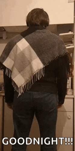 a man wearing a plaid scarf around his neck is standing in a kitchen and says goodnight .