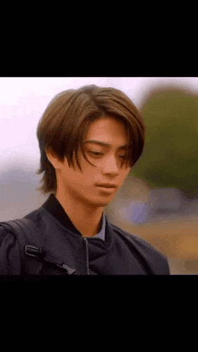 a young man wearing a black jacket and a backpack is looking down at something .