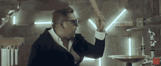 a man wearing sunglasses is playing drums in a dark room