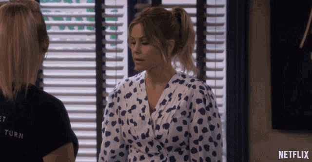 a woman in a polka dot robe stands next to another woman in a black shirt that says netflix on it