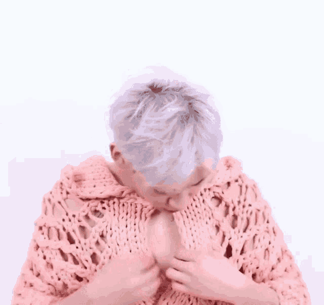 a man with white hair is wearing a pink sweater and looking down .