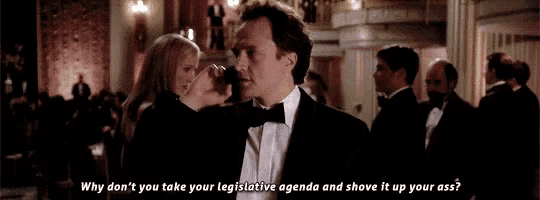 a man in a tuxedo is talking to a woman in a crowd while a woman holds his arm .