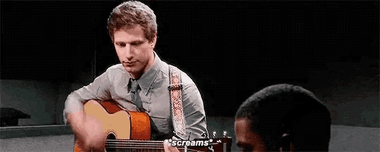 a man is playing a guitar in front of another man who is screaming .