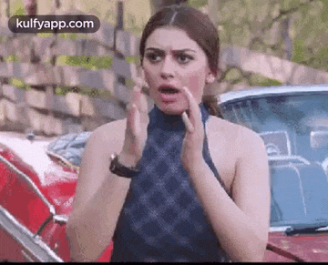 a woman is standing in front of a red car and making a surprised face .