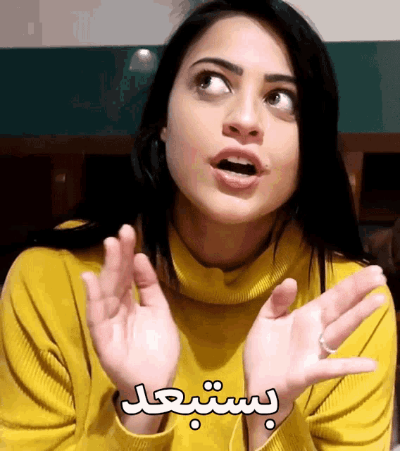 a woman wearing a yellow turtleneck sweater with arabic writing on it