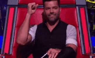 a man is sitting in a red chair with his fist up .