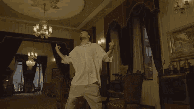 a man in a white shirt is standing in a room with a chandelier