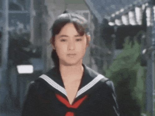a young woman in a school uniform with a red tie is standing on a city street .