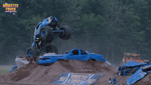 a blue monster truck is doing a trick on a dirt track